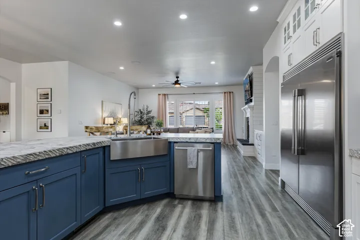 Kitchen featuring a farmhouse sink, stainless steel appliances, blue base cabinetry, white upper cabinetry, and wood-finish flooring