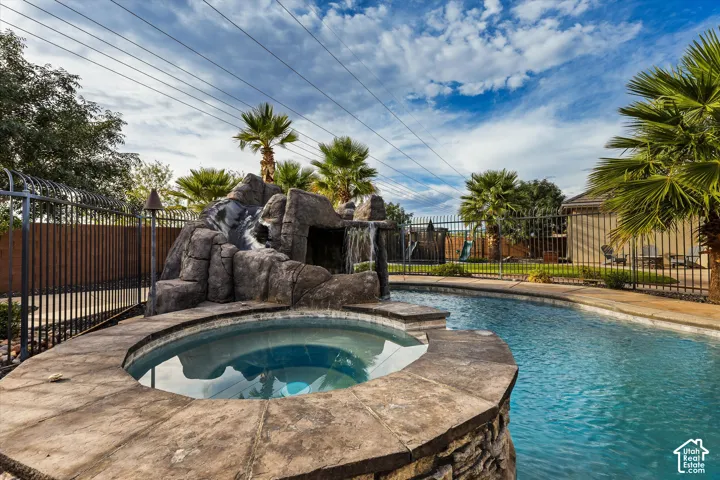 Swimming pool with rock waterfall feature, integrated spa, and palm trees