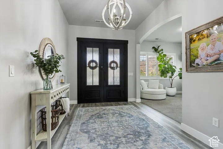 Double entry doors with frosted glass panels, wood-finish flooring, and a decorative orb chandelier