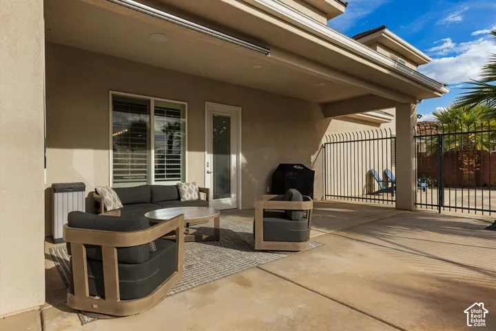 Covered outdoor patio with a concrete surface, featuring a glass-paned door, a window with horizontal blinds, and a black wrought-iron fence