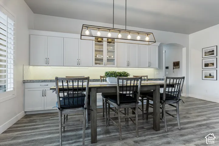 Wood-finish flooring, white shaker-style cabinetry, linear chandelier, diamond pattern backsplash, and custom window shutters