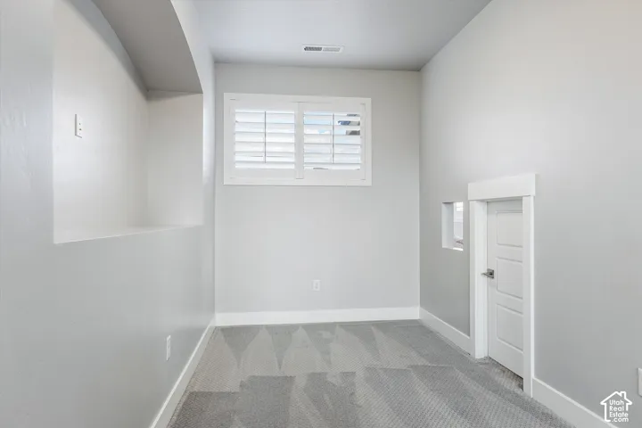 Recessed wall feature, window with plantation shutters, patterned carpet, white baseboards, and a secondary door
