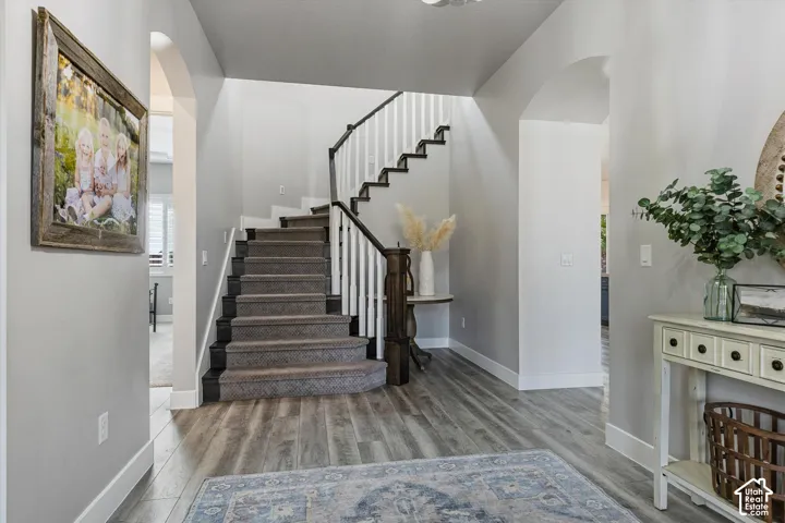 Wood-finish flooring, staircase with carpeted treads and white risers, arched doorways, and a console table with drawers