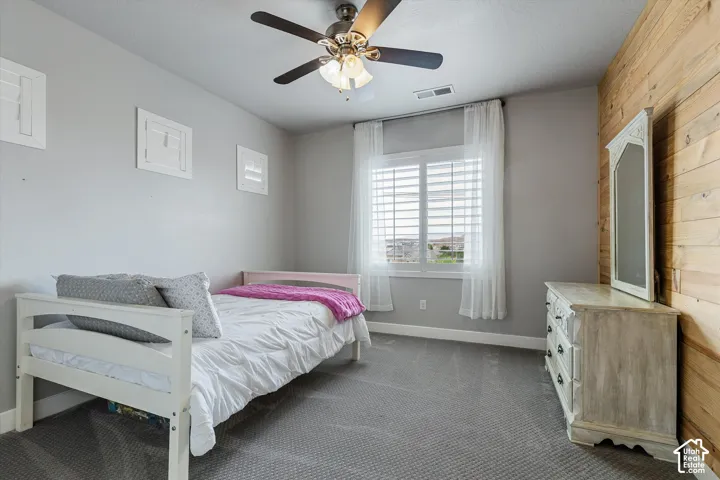Carpeted room featuring a window with plantation shutters, a wood accent wall, and a ceiling fan with integrated lighting