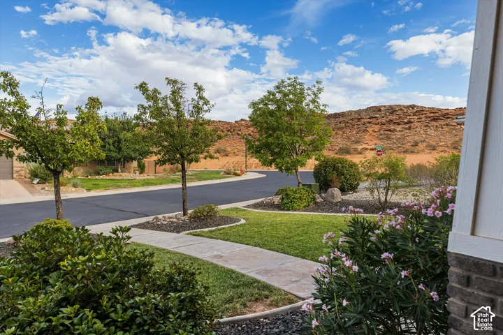 Landscaped front yard with green lawn, flowering shrubs, mature trees, and a concrete pathway
