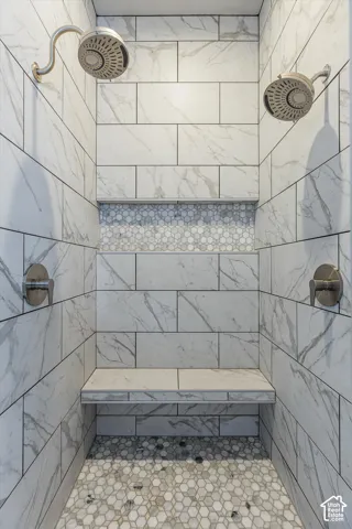 Dual shower heads, tiled shower walls, mosaic tile accent, built-in shower bench, and hexagonal floor tile