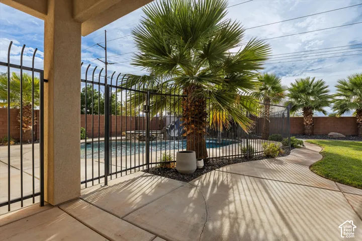 Expansive backyard featuring a manicured lawn, a swimming pool with a black wrought iron fence, a concrete patio, and mature palm trees