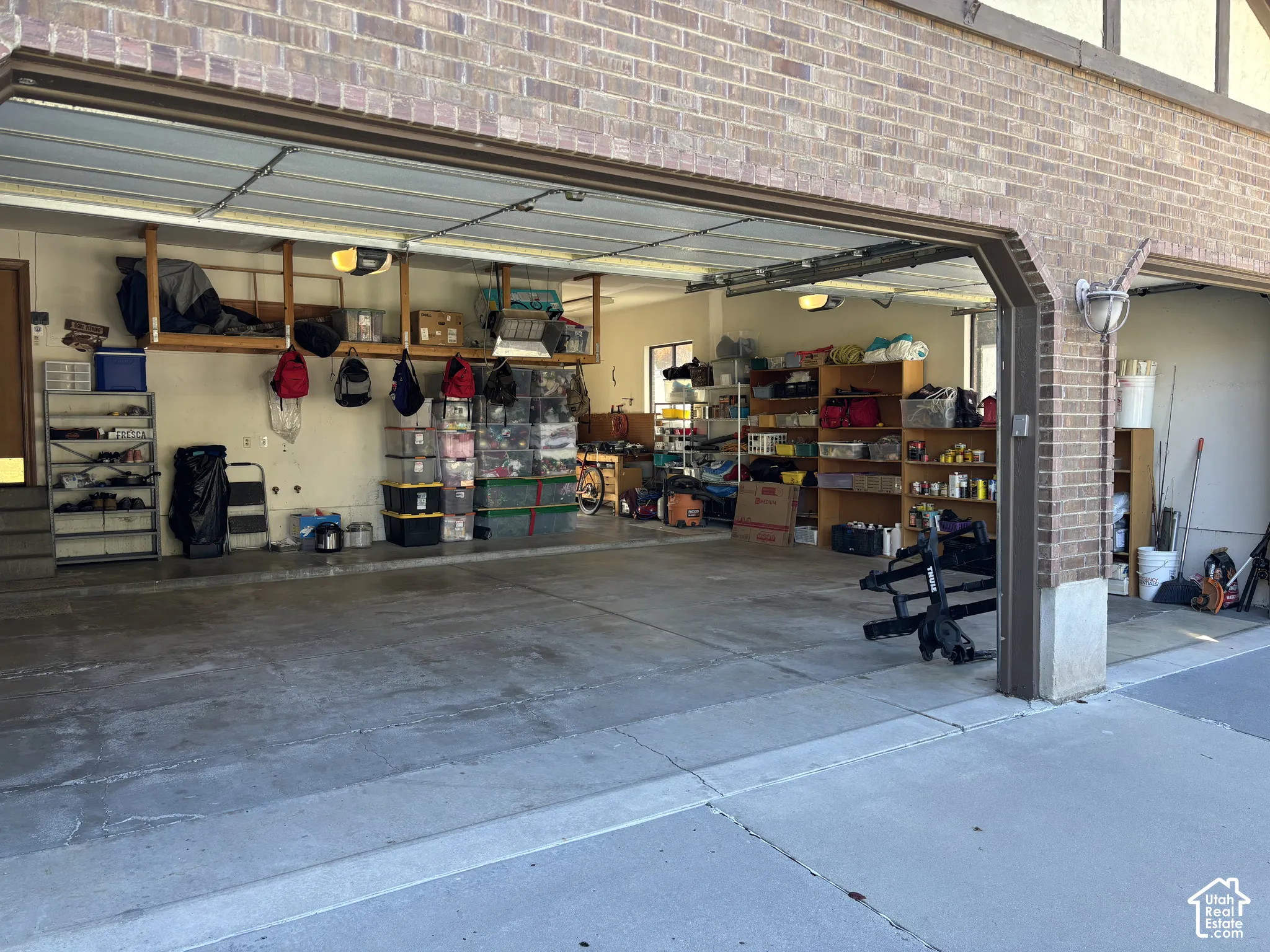 Brick facade garage with concrete flooring, built-in shelving, and overhead storage