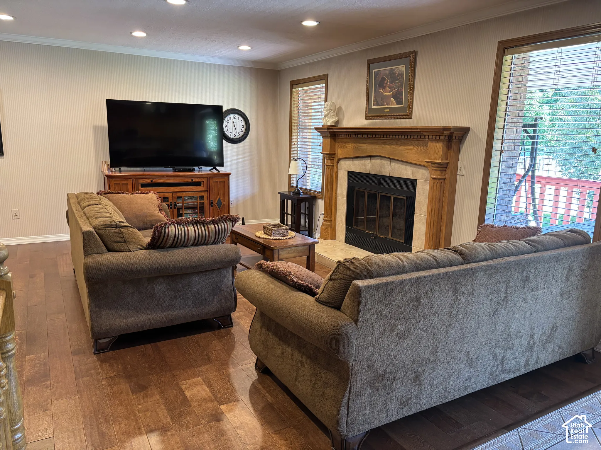 Warm wood-finish flooring throughout, a fireplace with a detailed wood mantle and stone surround, and recessed lighting
