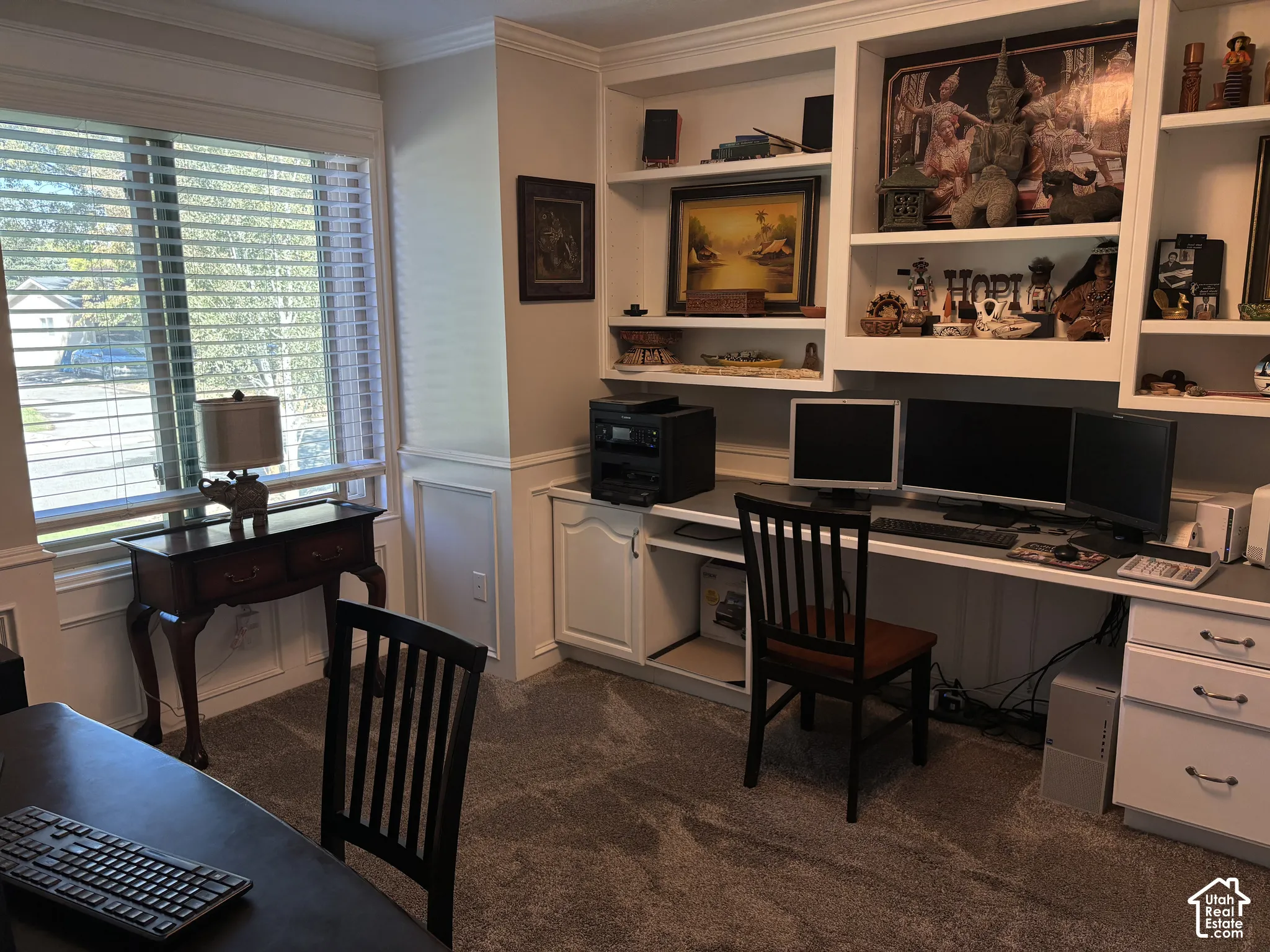 Built-in shelving, integrated desk, window with horizontal blinds, wainscoting, and carpeted flooring