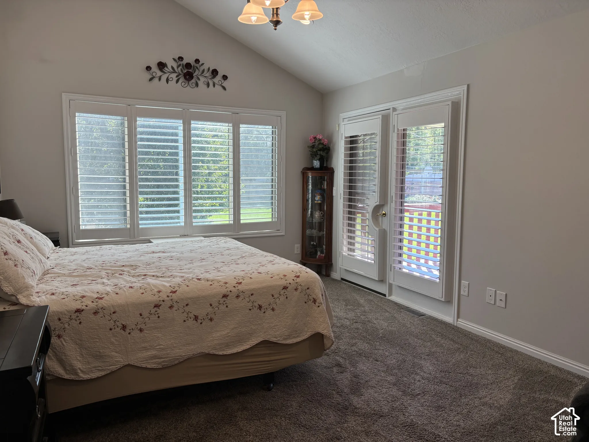 Vaulted ceiling, ceiling-mounted light fixture, white window shutters, double French doors, and soft gray carpeting