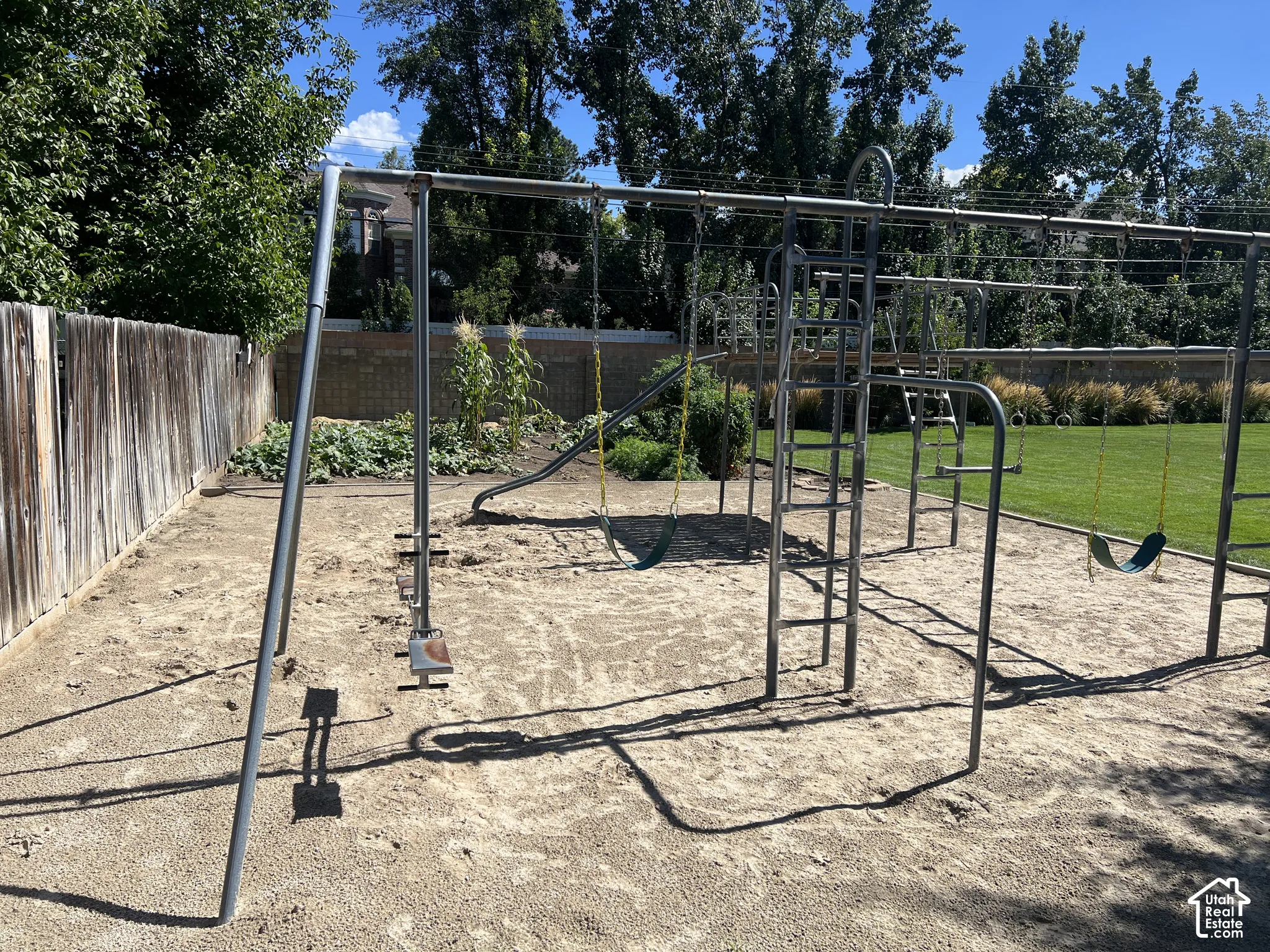 Backyard area featuring a playground structure with swings and a slide, a wooden fence, and a manicured lawn