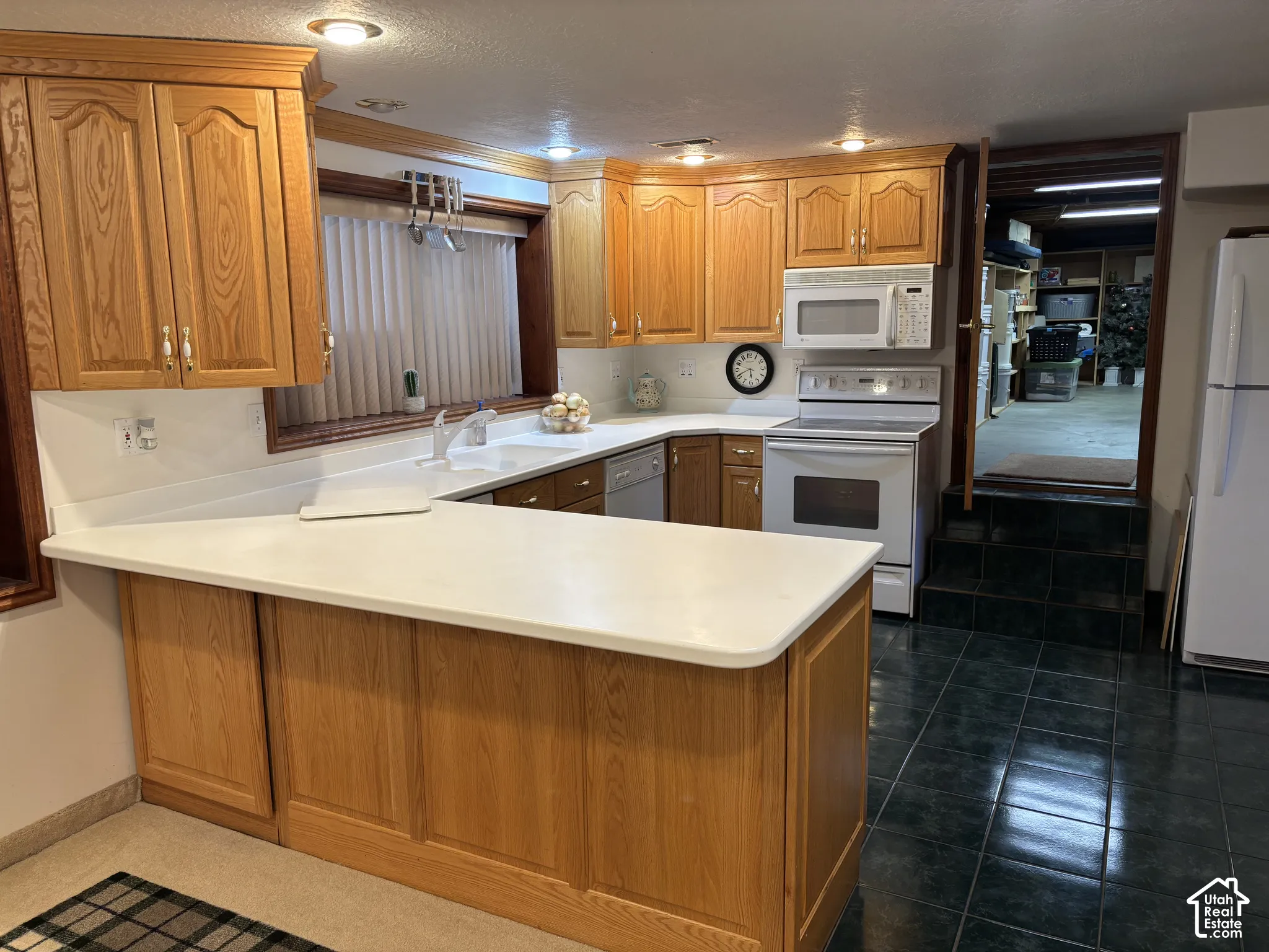 Wood-finish cabinetry with white countertops, integrated sink, and white appliances