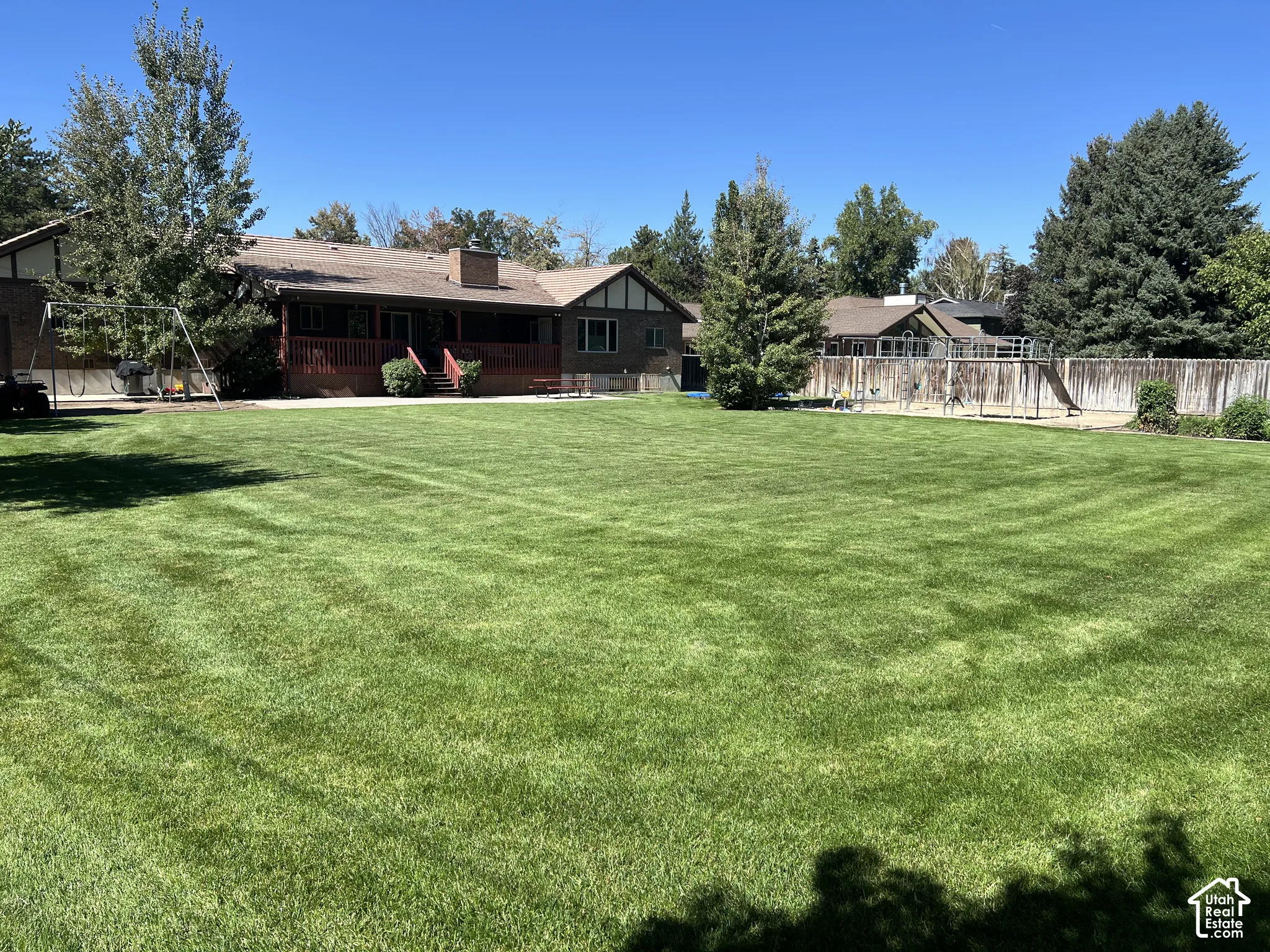 Expansive backyard featuring a manicured lawn, mature trees, a wood-sided fence, and a multi-level deck with steps