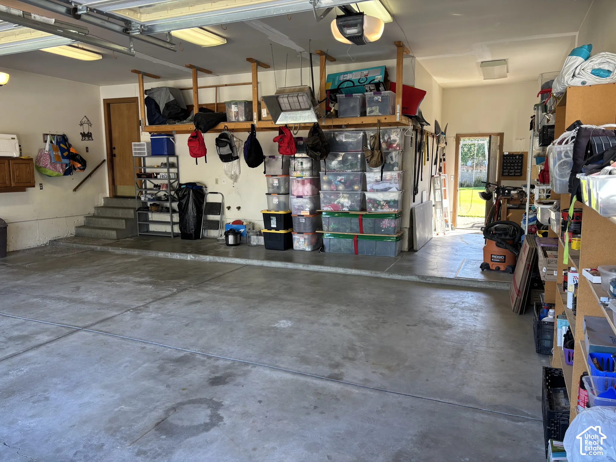 Concrete flooring with overhead lighting, built-in shelving, and garage door opener