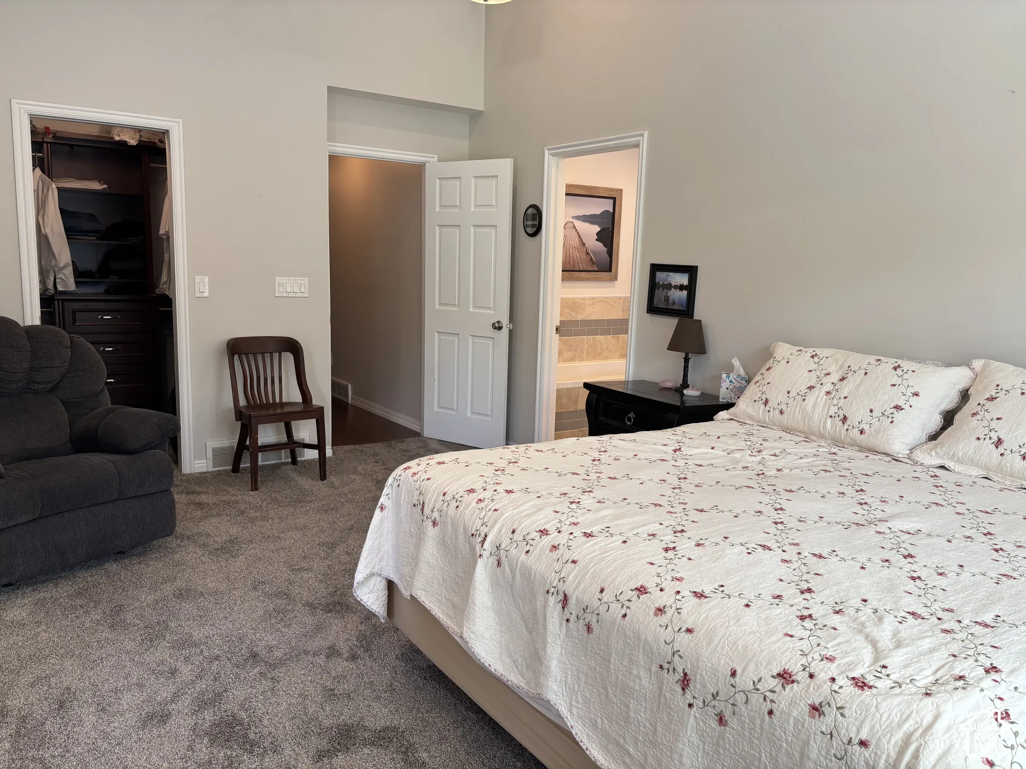 Plush gray carpeting throughout, featuring a built-in closet system with dark wood-finish cabinetry, and a private attached bath with tiled walls