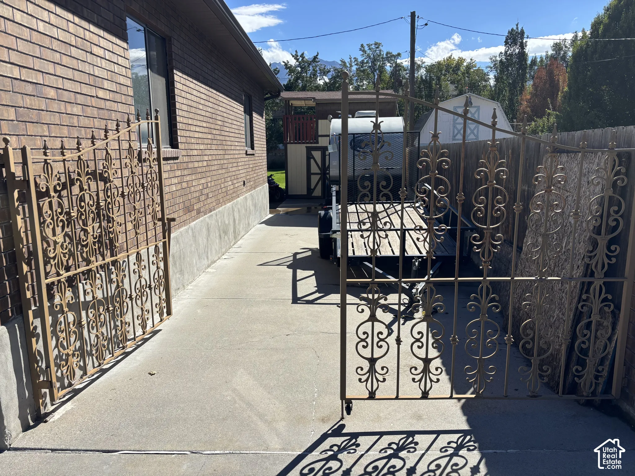 Brick exterior with concrete foundation, ornamental iron gates, concrete pathway, and a detached storage shed