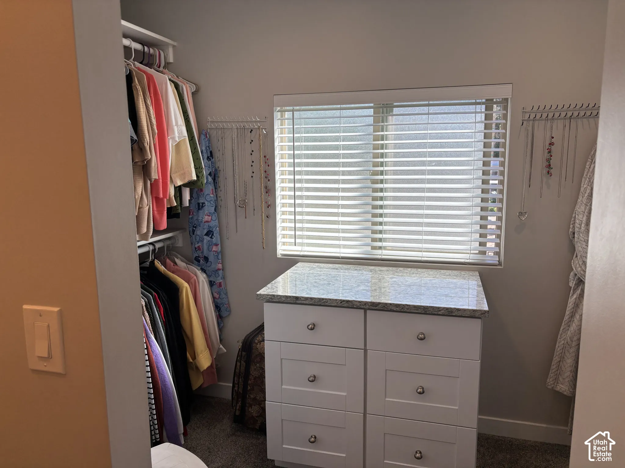 Built-in storage island with a stone-finish countertop, white cabinetry with metal hardware, and a window with horizontal blinds