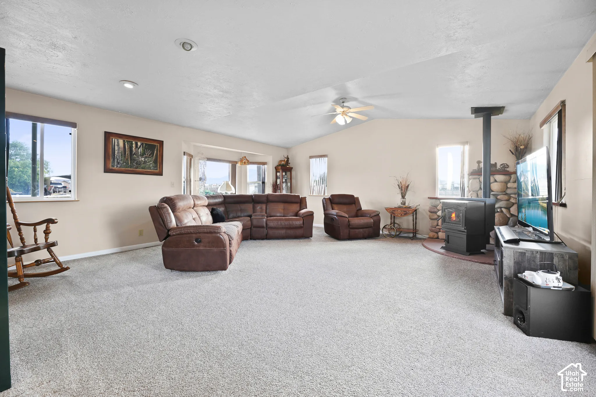 Spacious living area featuring a stone accent wall, a wood-burning stove, a vaulted ceiling, recessed lighting, and multiple windows