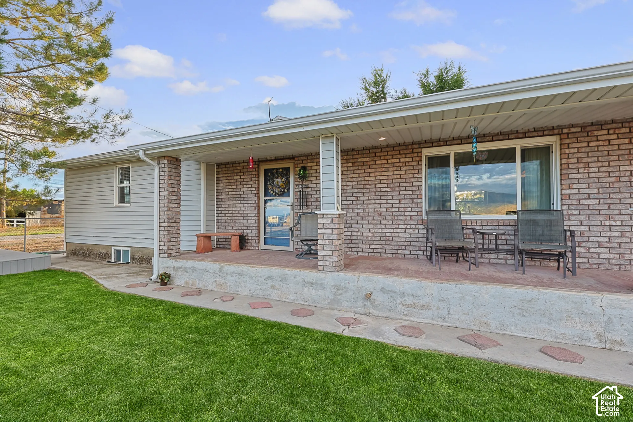 Brick and siding exterior with a covered concrete porch, featuring a manicured lawn and decorative stepping stones