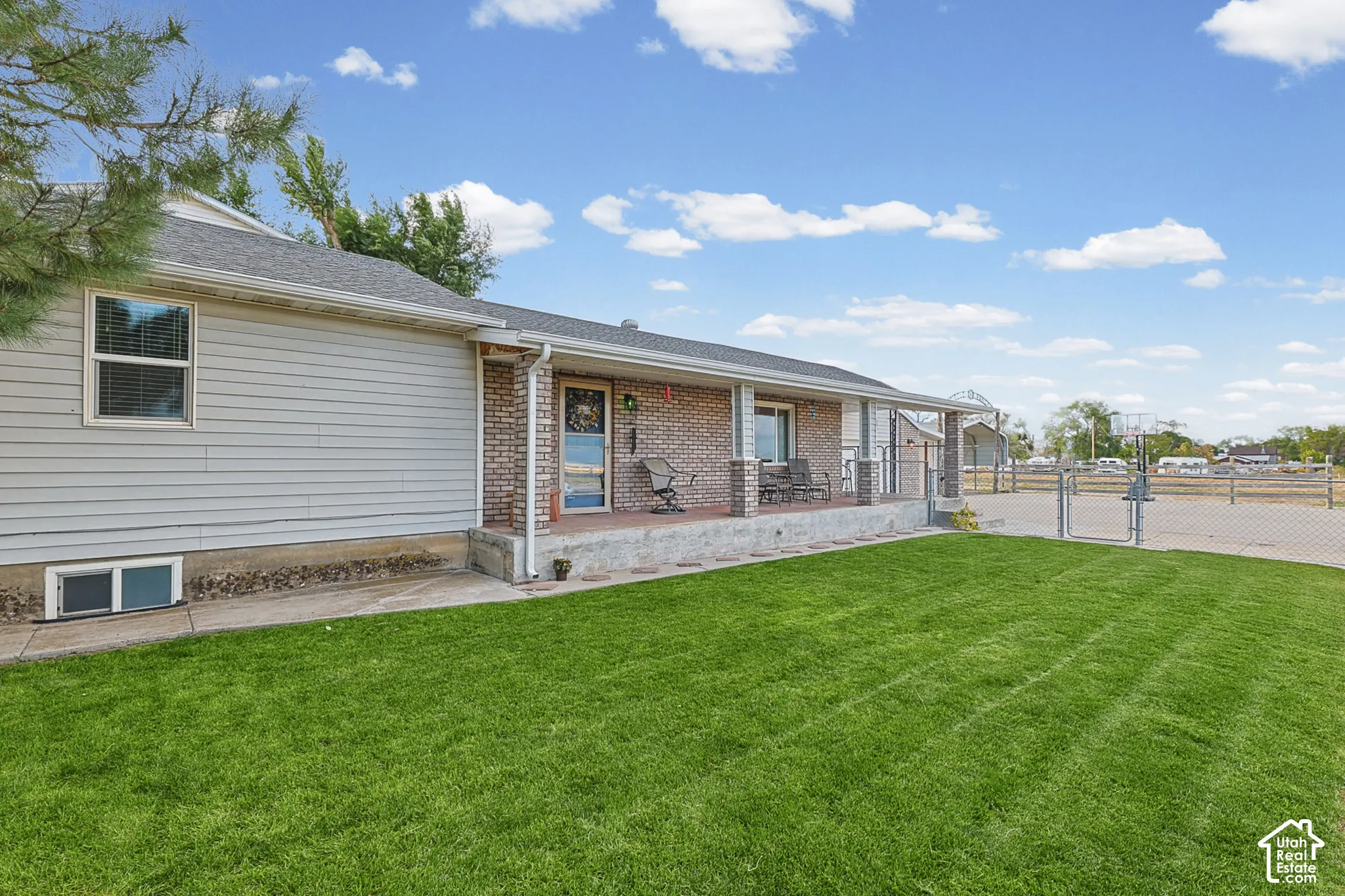 Expansive front lawn with a concrete walkway, elevated covered porch with brick columns, and a chain-link fence