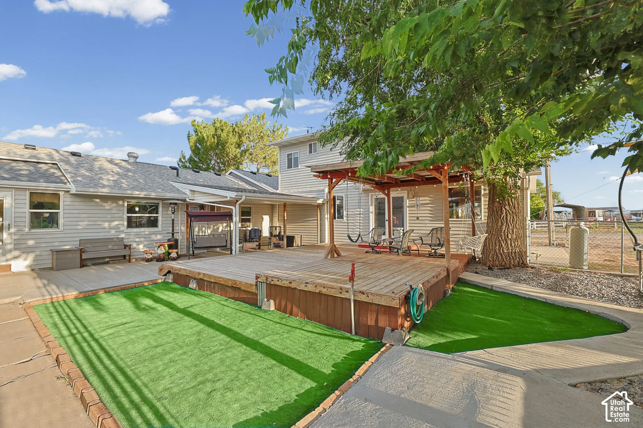 Expansive wood deck with a pergola, artificial turf area, and mature trees