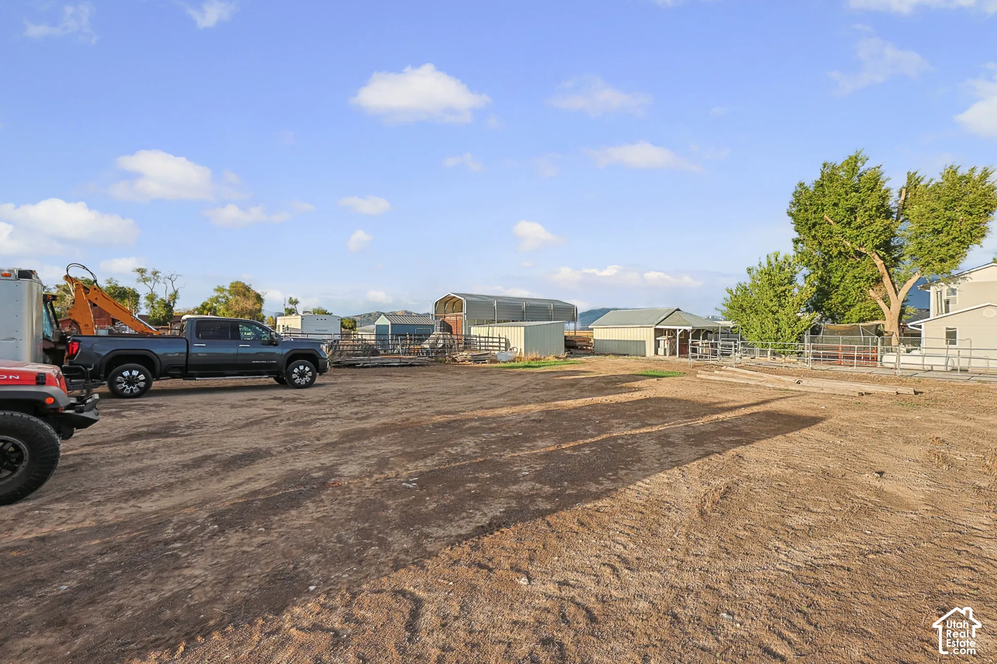 Expansive dirt lot with various outbuildings and mature trees