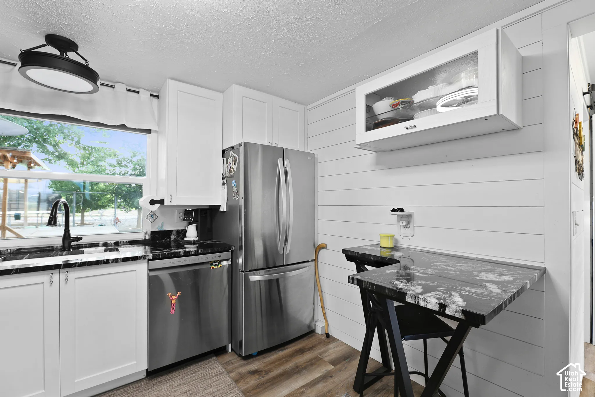 White shaker cabinetry, black stone-finish countertops, stainless steel appliances, wood-finish flooring, and shiplap paneling