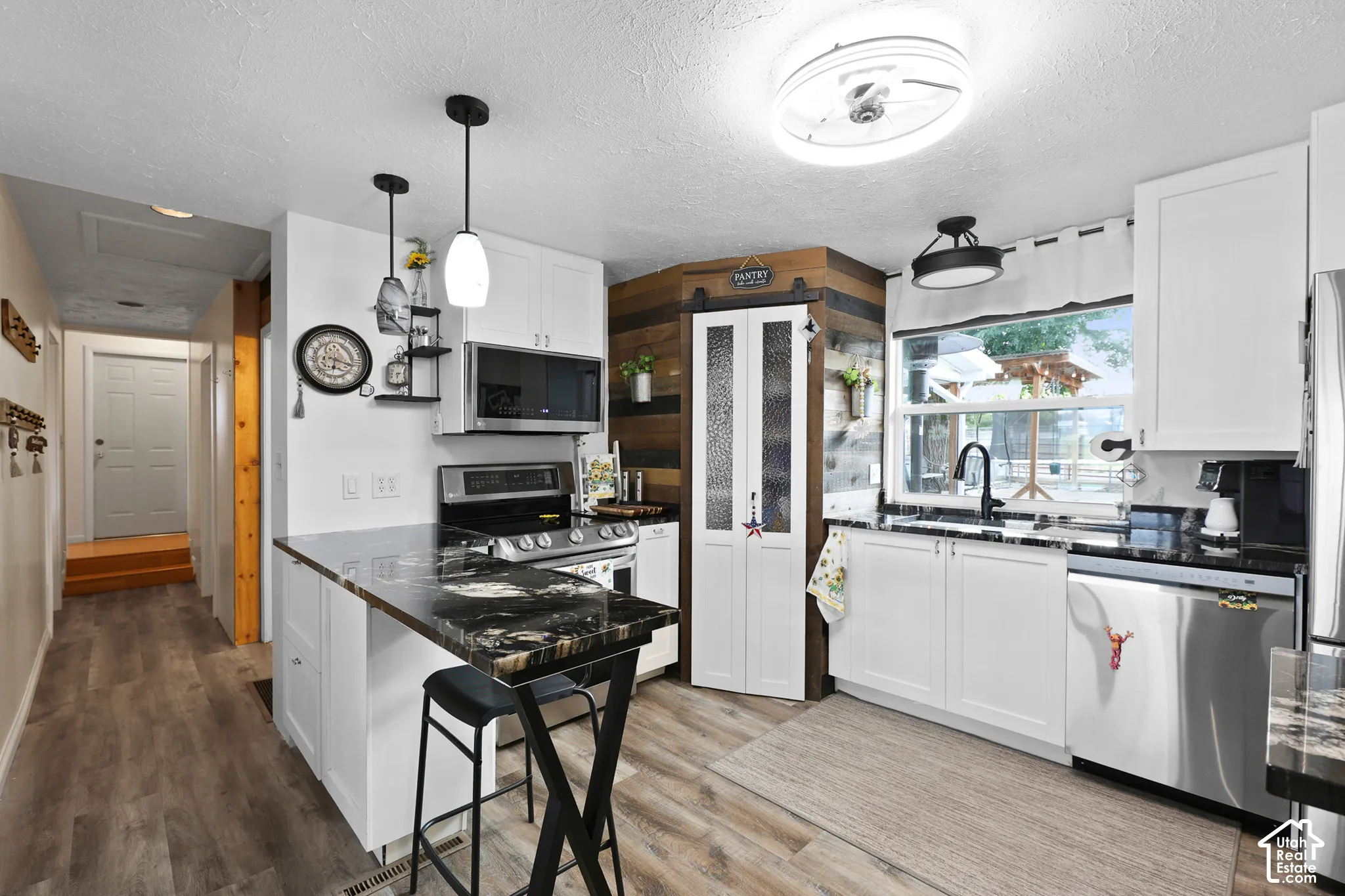 White cabinetry with black countertops, stainless steel appliances, and a wood-paneled accent wall