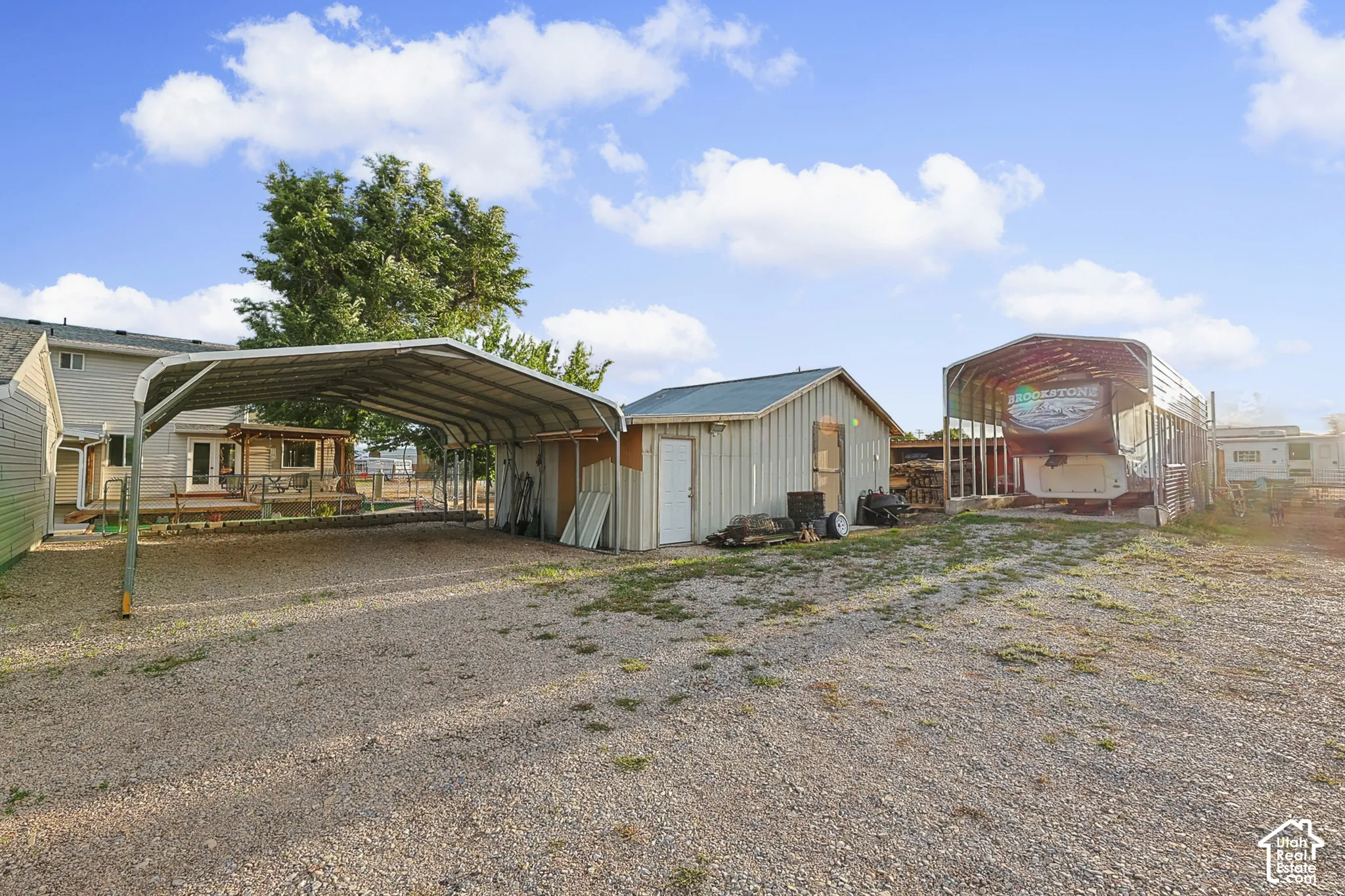 Gravel surface with multiple metal carports, a detached shed, and a rear deck