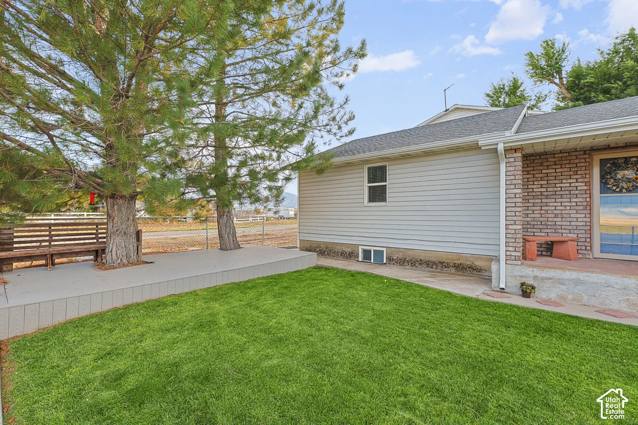 Manicured lawn, elevated patio, mature trees, brick facade, and vinyl siding