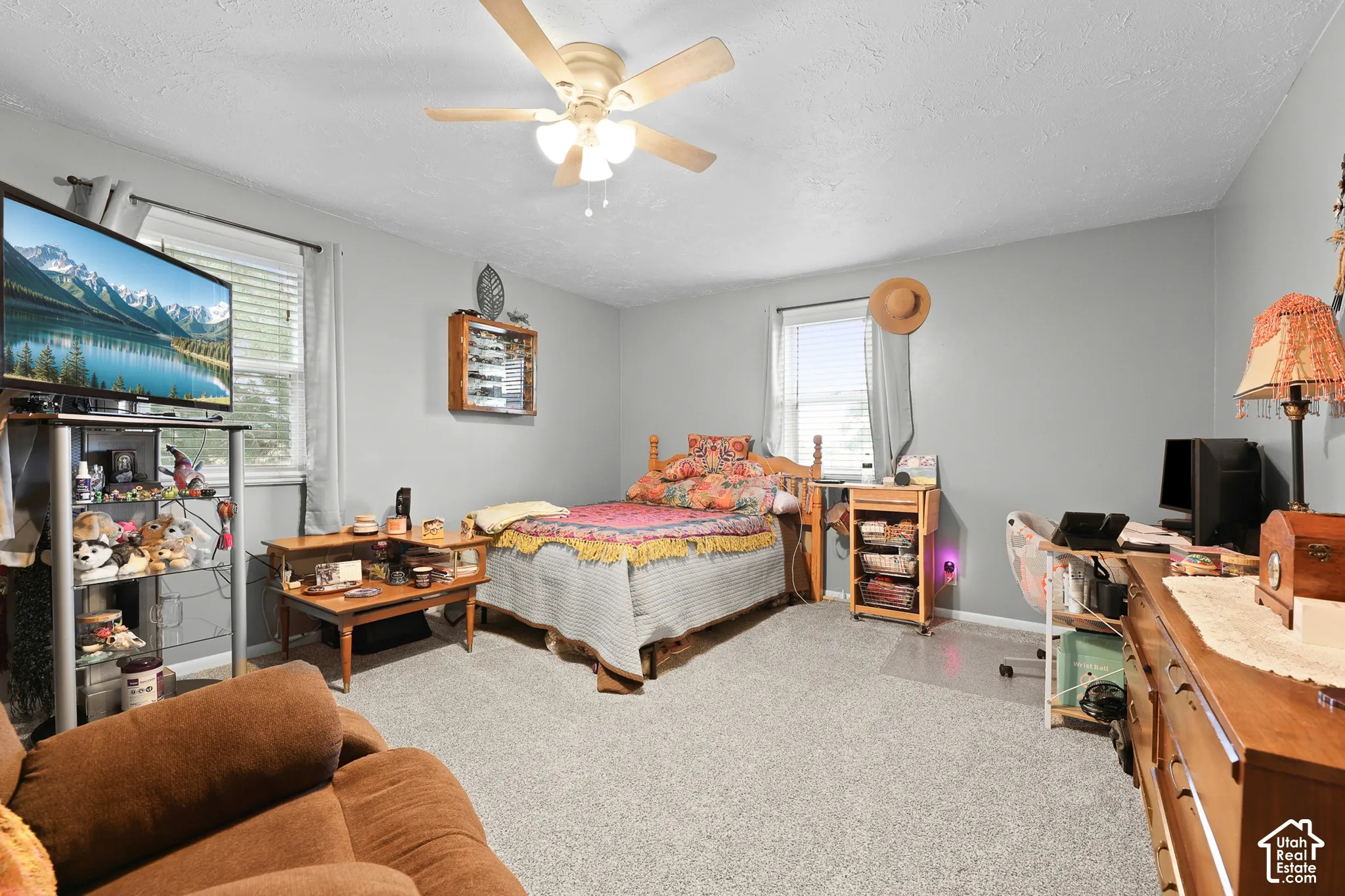 Textured ceiling, ceiling fan with light fixture, light gray walls, carpet flooring, and a large window with blinds