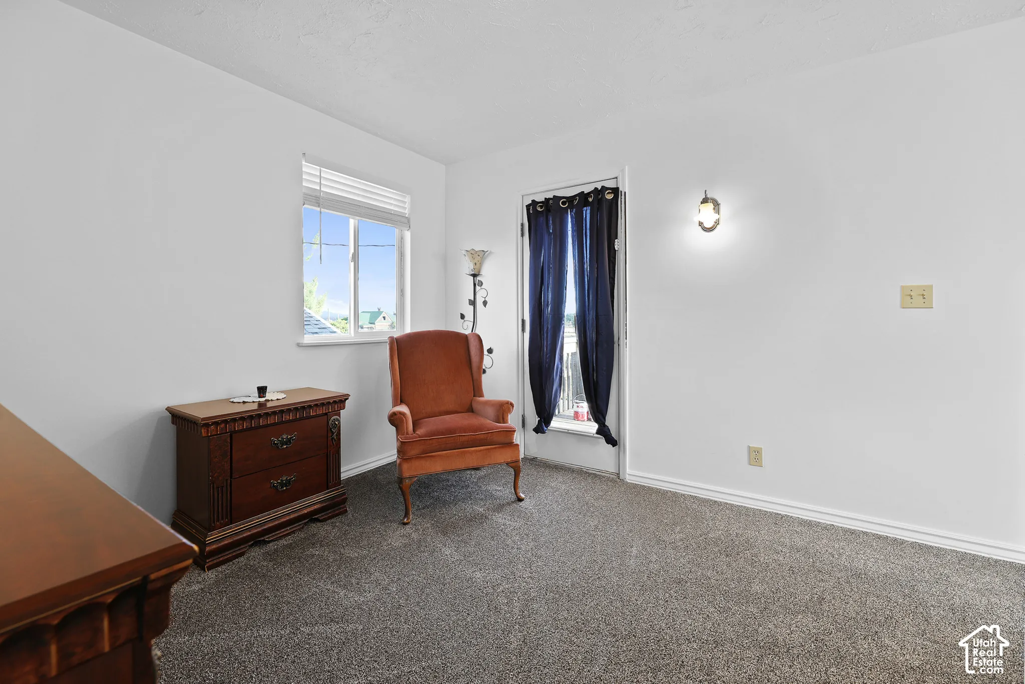 Neutral tone wall paint, carpeted flooring, window with blinds, and built-in wall sconce