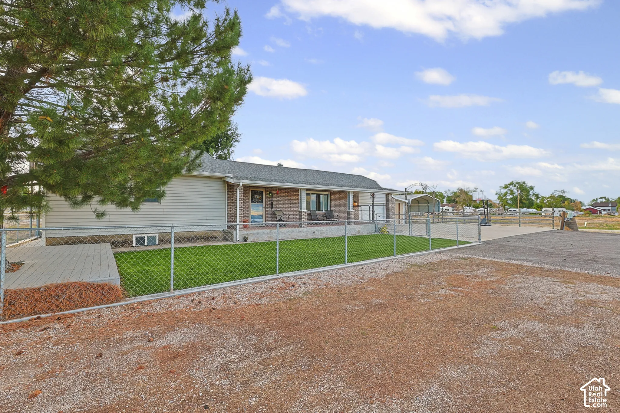 Ranch-style residence featuring a covered front porch with columns, a chain-link fence enclosing a manicured lawn, and a graveled driveway