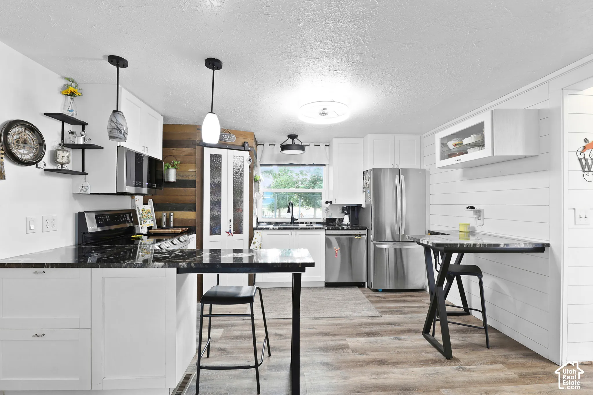 White cabinetry, stainless steel appliances, dark countertops, wood-finish flooring, and shiplap accents
