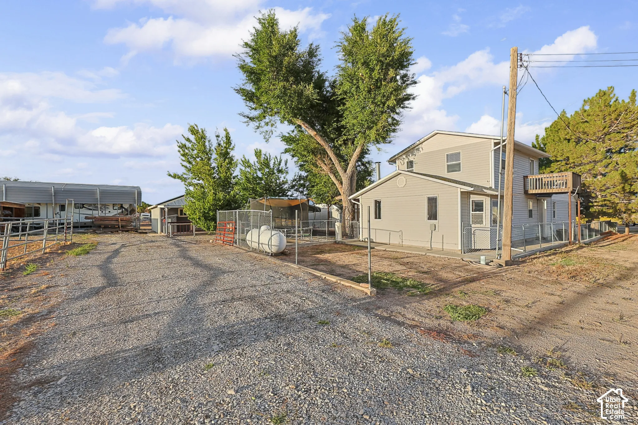 Two-story residence with a side balcony, gravel driveway, and multiple outbuildings