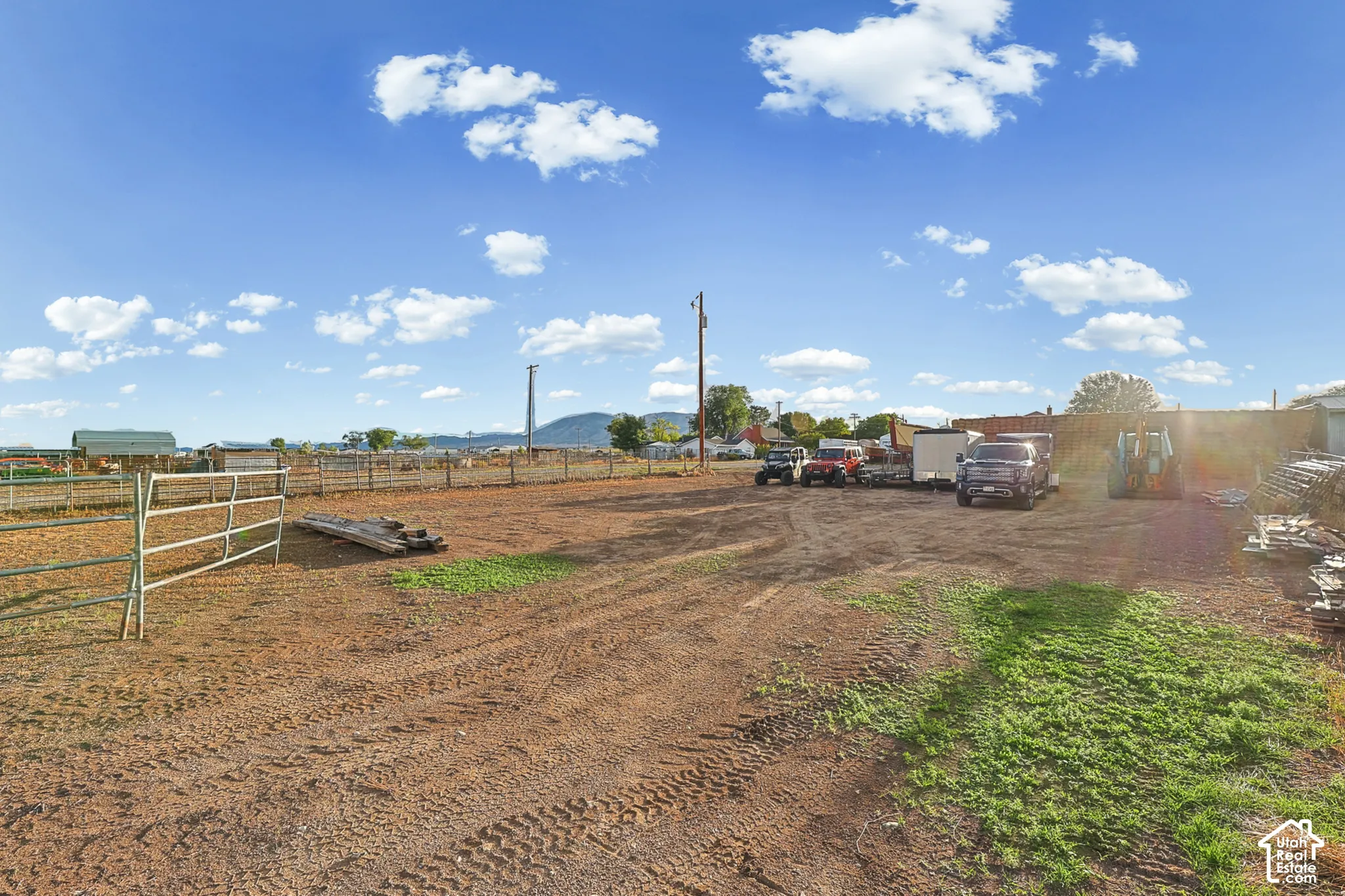 Expansive open dirt area with perimeter fencing, featuring a metal gate and distant structures