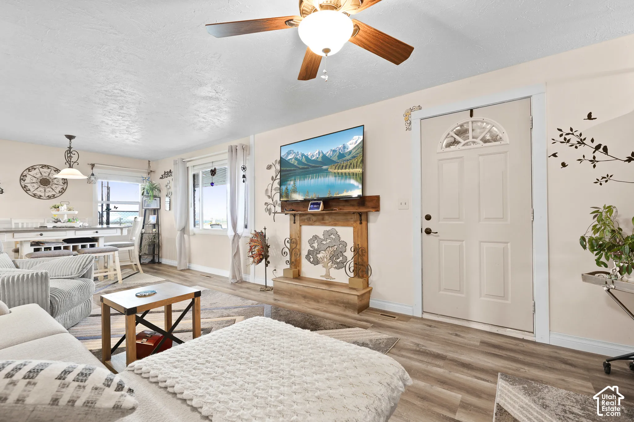 Wood-finish flooring throughout, ceiling fan with integrated lighting, wood-finish mantel, and white paneled entry door with an arched window insert