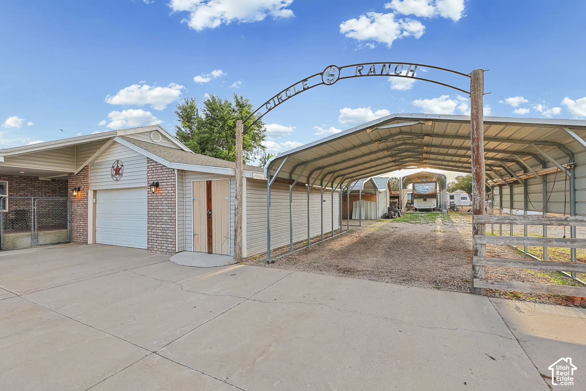 Concrete driveway, attached garage with brick-finish siding, separate storage shed, and a large metal carport structure