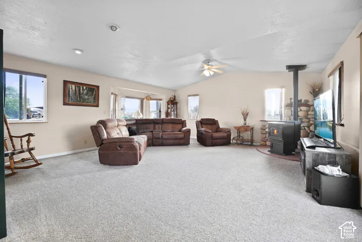Spacious living area featuring a stone accent wall, a wood-burning stove, a vaulted ceiling, recessed lighting, and multiple windows