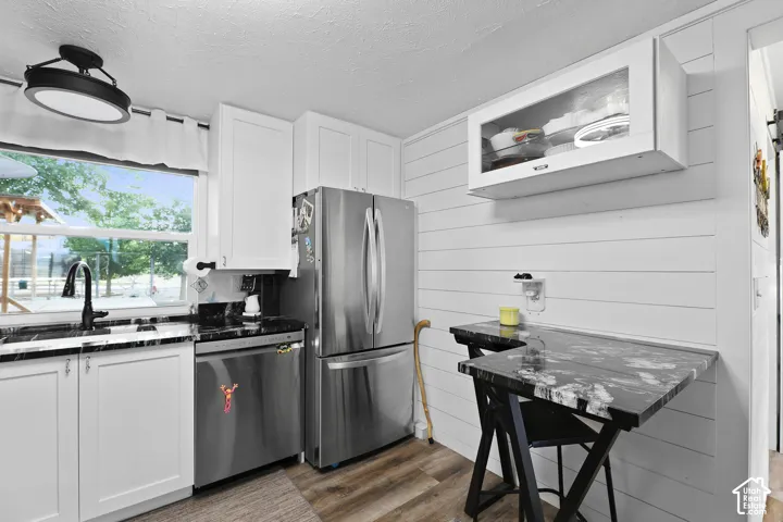 White shaker cabinetry, black stone-finish countertops, stainless steel appliances, wood-finish flooring, and shiplap paneling