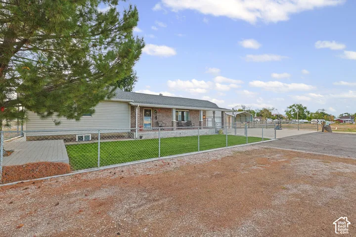Ranch-style residence featuring a covered front porch with columns, a chain-link fence enclosing a manicured lawn, and a graveled driveway