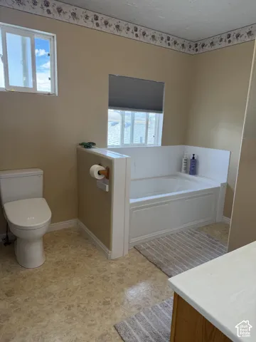 Built-in bathtub, dual windows, neutral wall tones, patterned flooring, and a white toilet