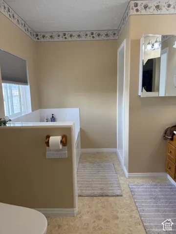 Built-in bathtub with tiled surround, neutral wall paint, vanity with integrated lighting, and patterned flooring