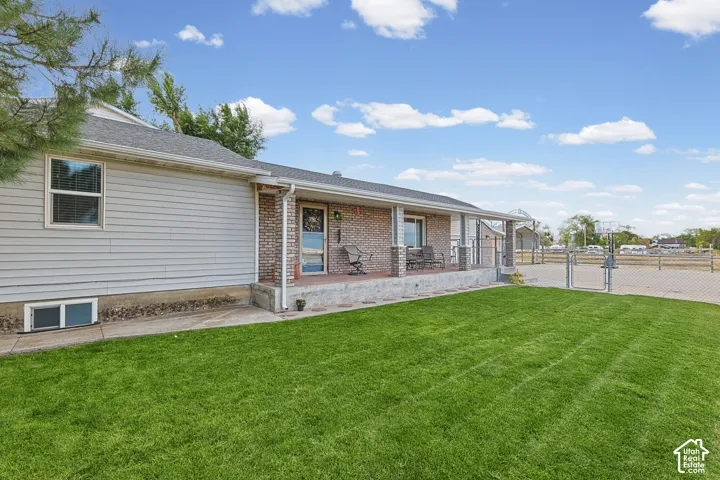 Expansive front lawn with a concrete walkway, elevated covered porch with brick columns, and a chain-link fence