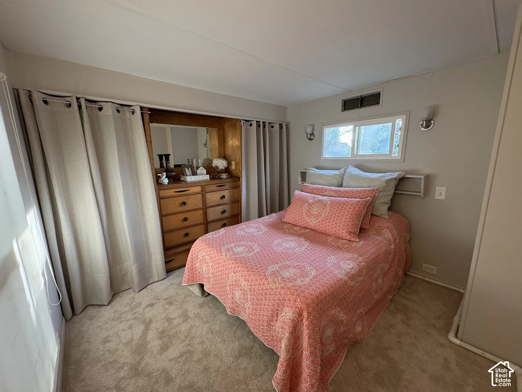 Built-in wooden dresser with mirror, light-colored wall-to-wall carpeting, recessed window, and wall-mounted sconces