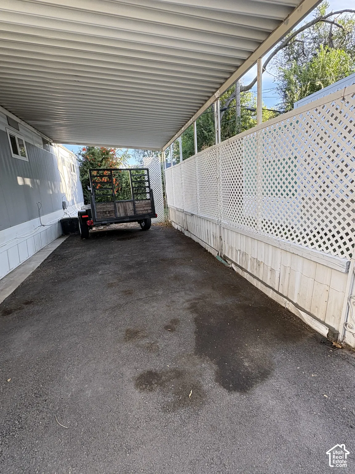Carport featuring a corrugated metal roof, white lattice fencing, and a paved surface