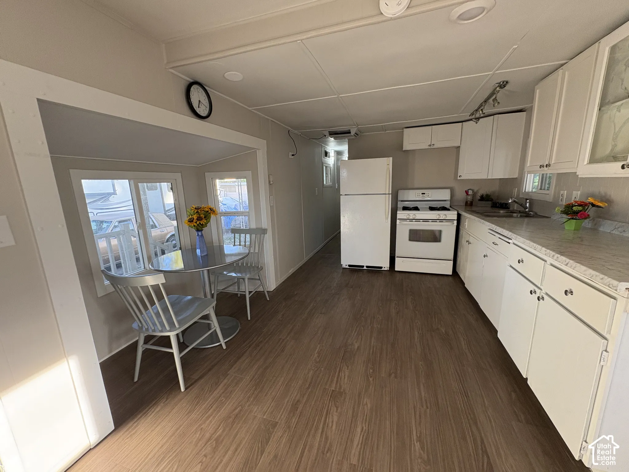 Kitchen with wood-finish flooring, white cabinetry, a built-in sink, and white appliances
