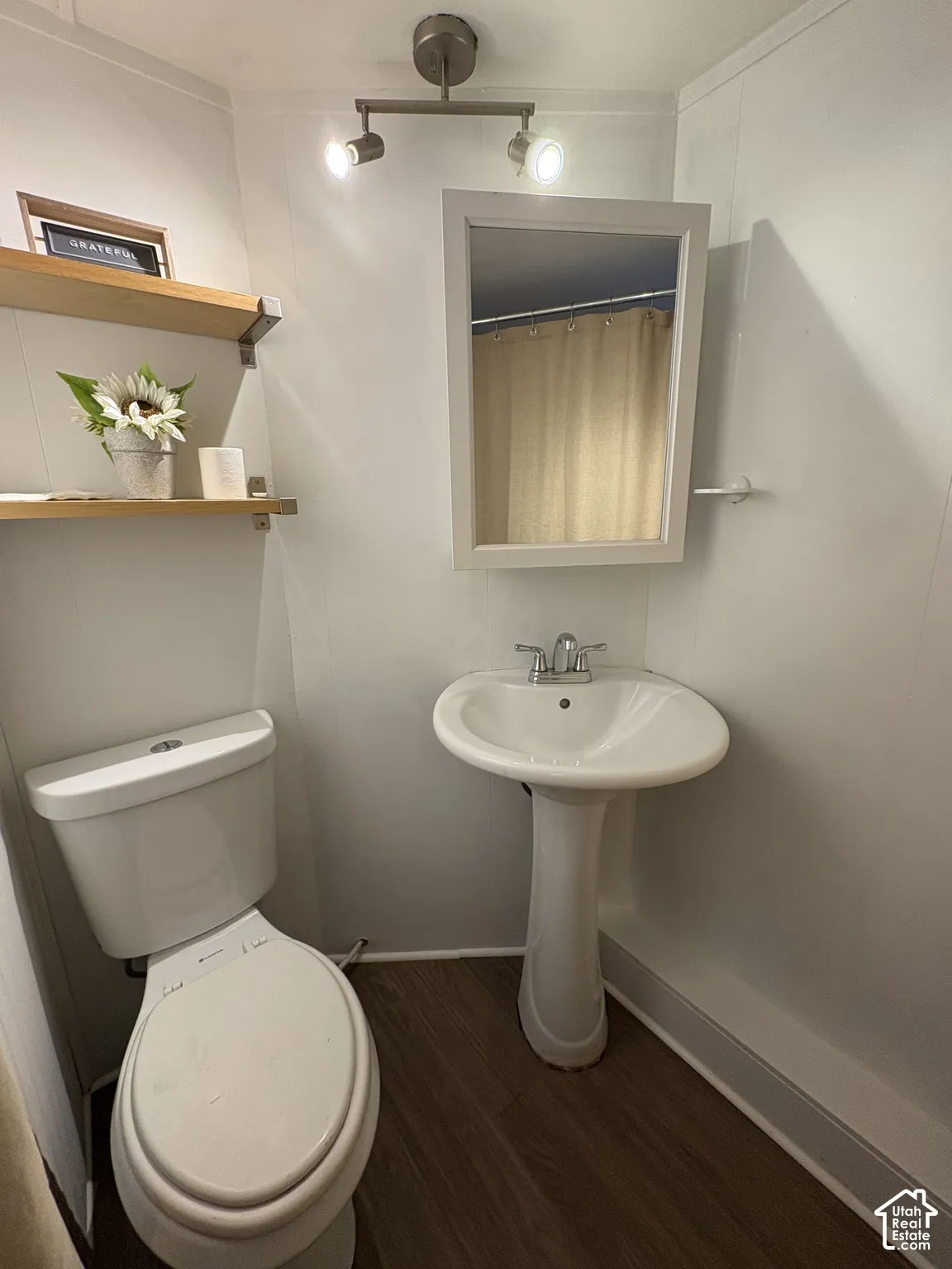 Pedestal sink with chrome faucet, wall-mounted mirror, wood-finish flooring, and recessed ceiling lighting