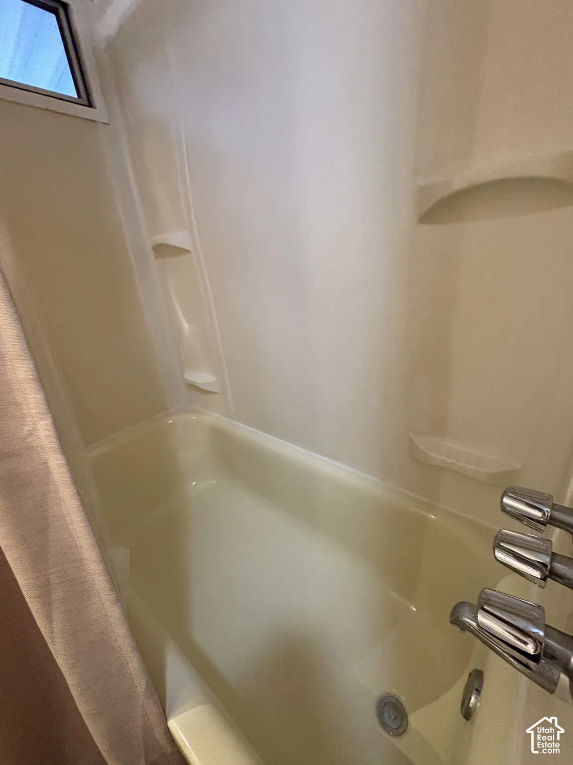 White fiberglass tub and shower combination with chrome fixtures and built-in shelving